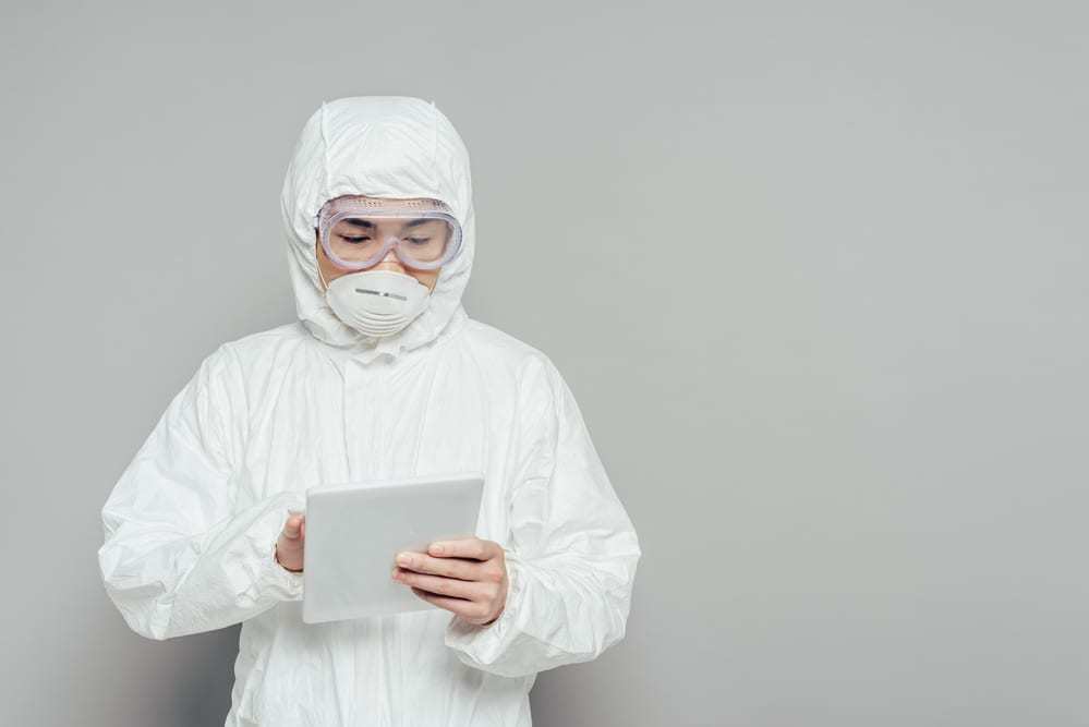 Healthcare worker in PPE using tablet in front of gray background