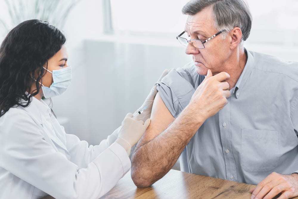 Older Man Receiving Vaccine Injection from Young Healthcare Worker Wearing Face Mask