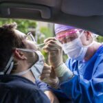 Health care worker in protective gear taking a nasal swab of a man in a car