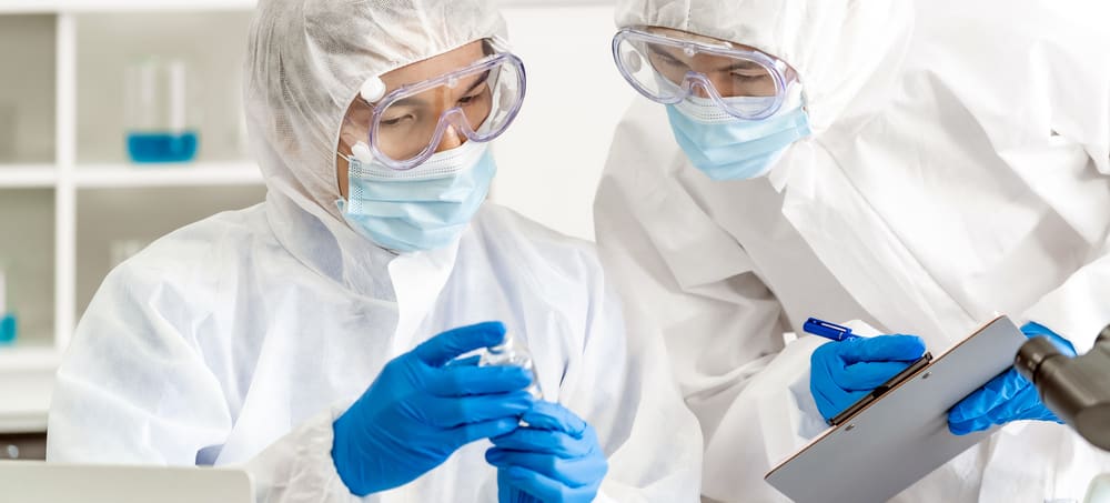 Two scientists in PPE examine vaccine, write on clipboard