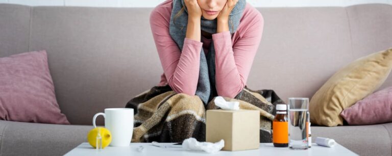 Young woman on couch, ill, with tissues, medicine, water, and tea in front of her