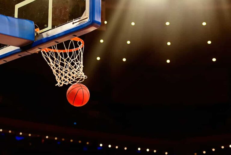 Basketball having just passed through basket in dark arena