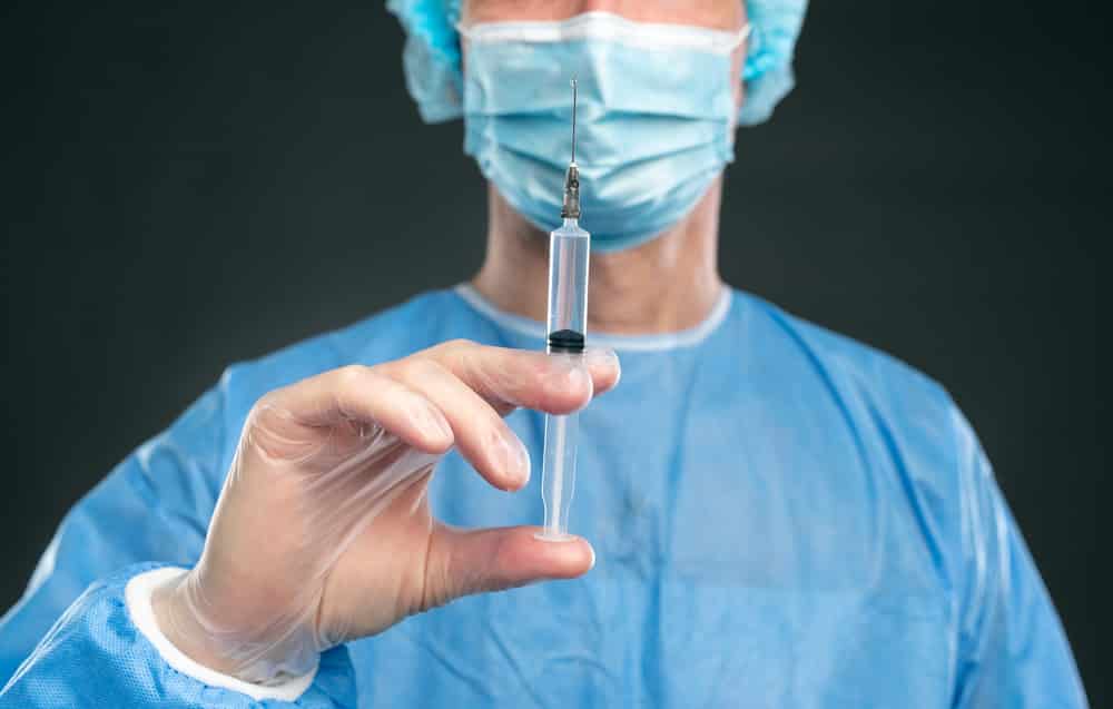 Close-up of vaccine syringe held by doctor wearing face mask