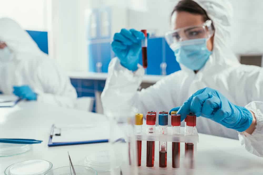 Medical researcher wearing PPE holding up test tube with blood sample