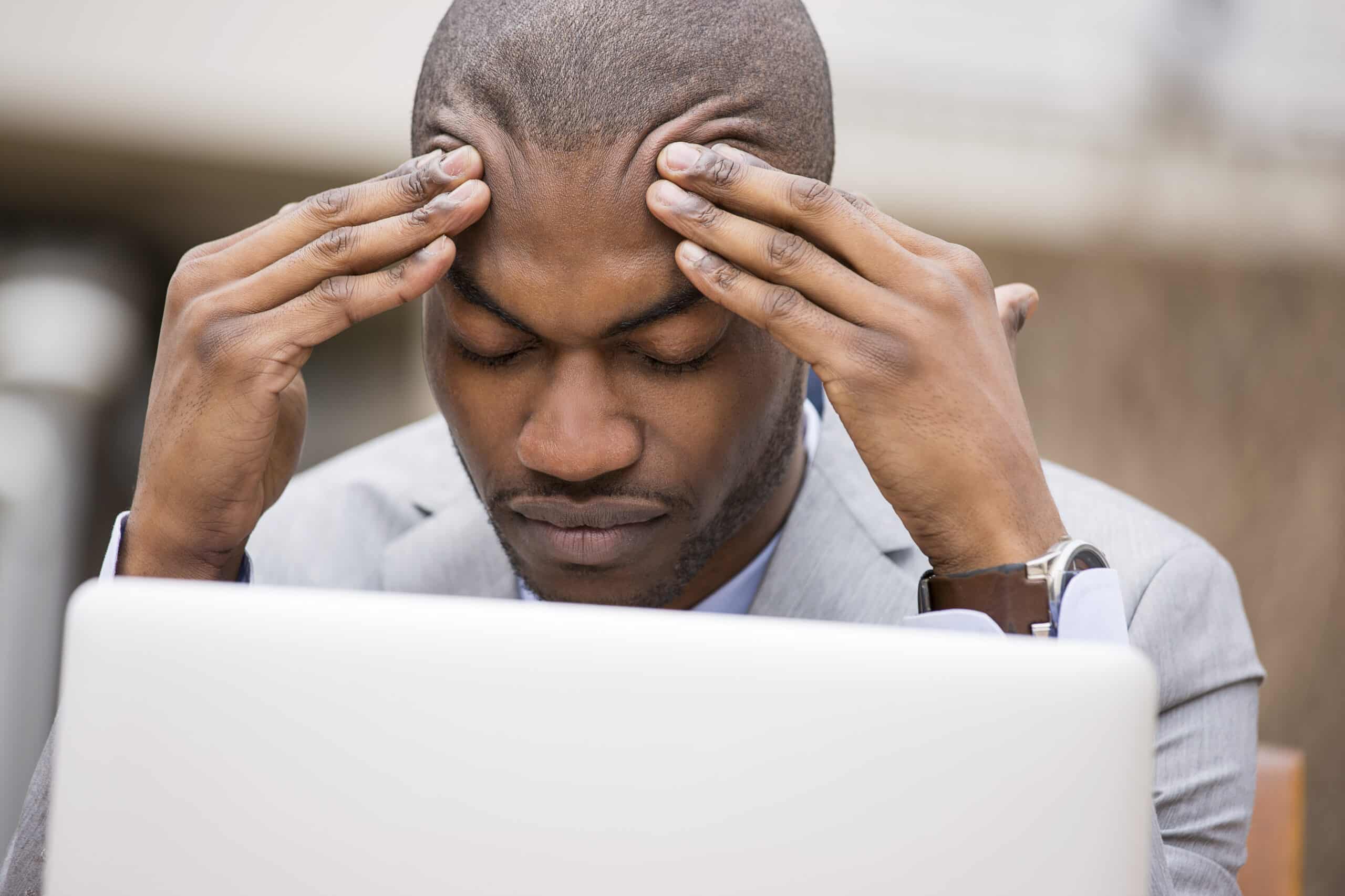 Stressed young man rubbing forehead in front of laptop