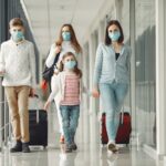 Family wearing face masks at the airport, rolling luggage