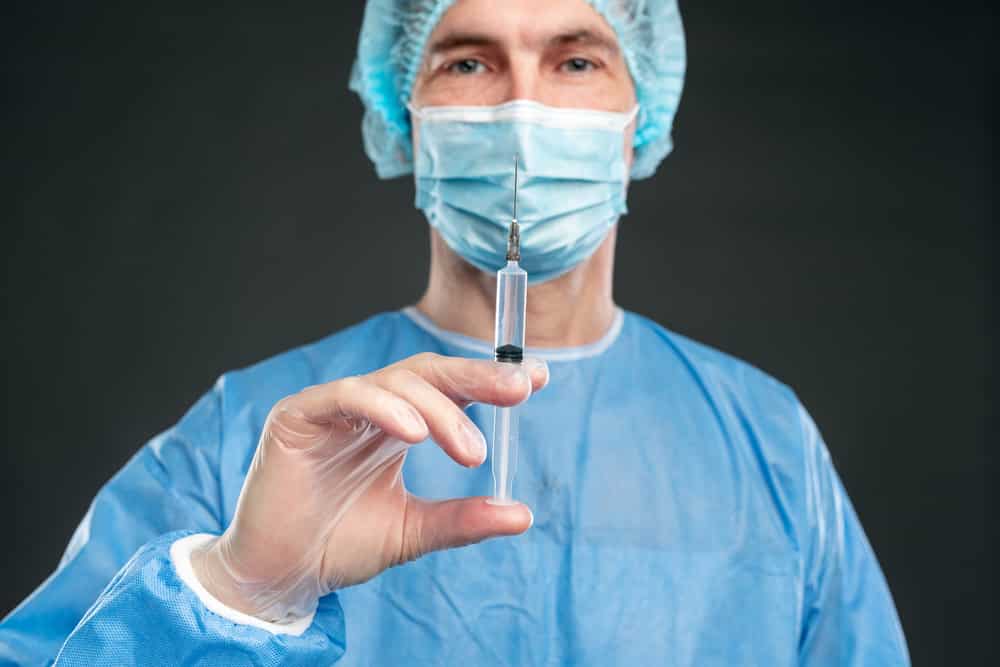 Male-doctor-in-protective-suit-holding-up-vaccine