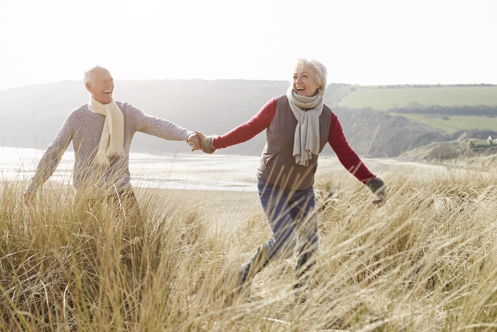 Happy older couple watching hand in hand in beach dunes