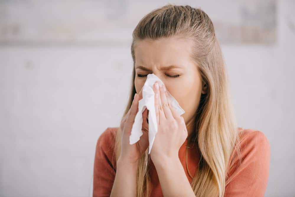 Woman sneezing, holding tissue to nose