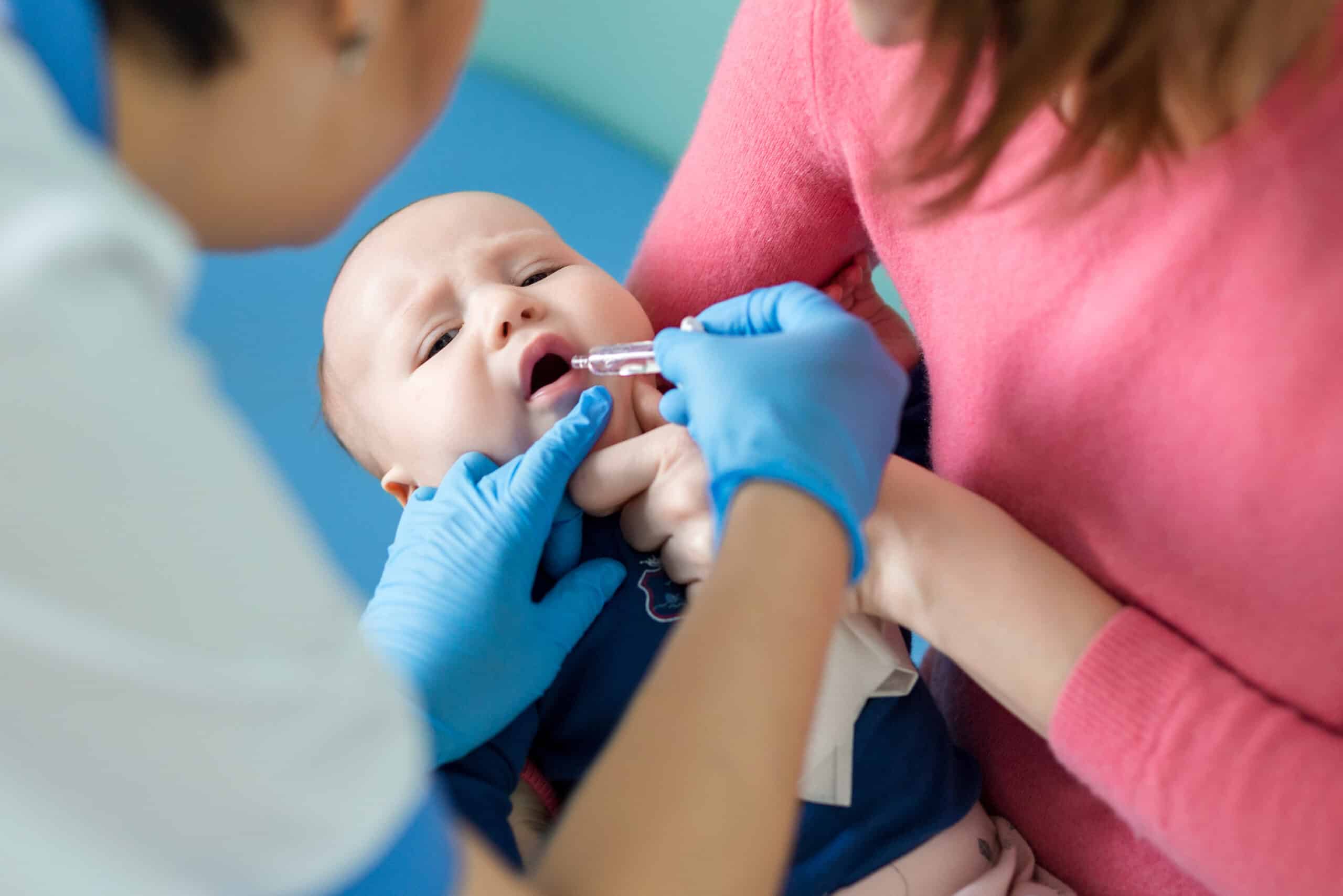 Nurse giving baby an oral vaccine while mother holds baby