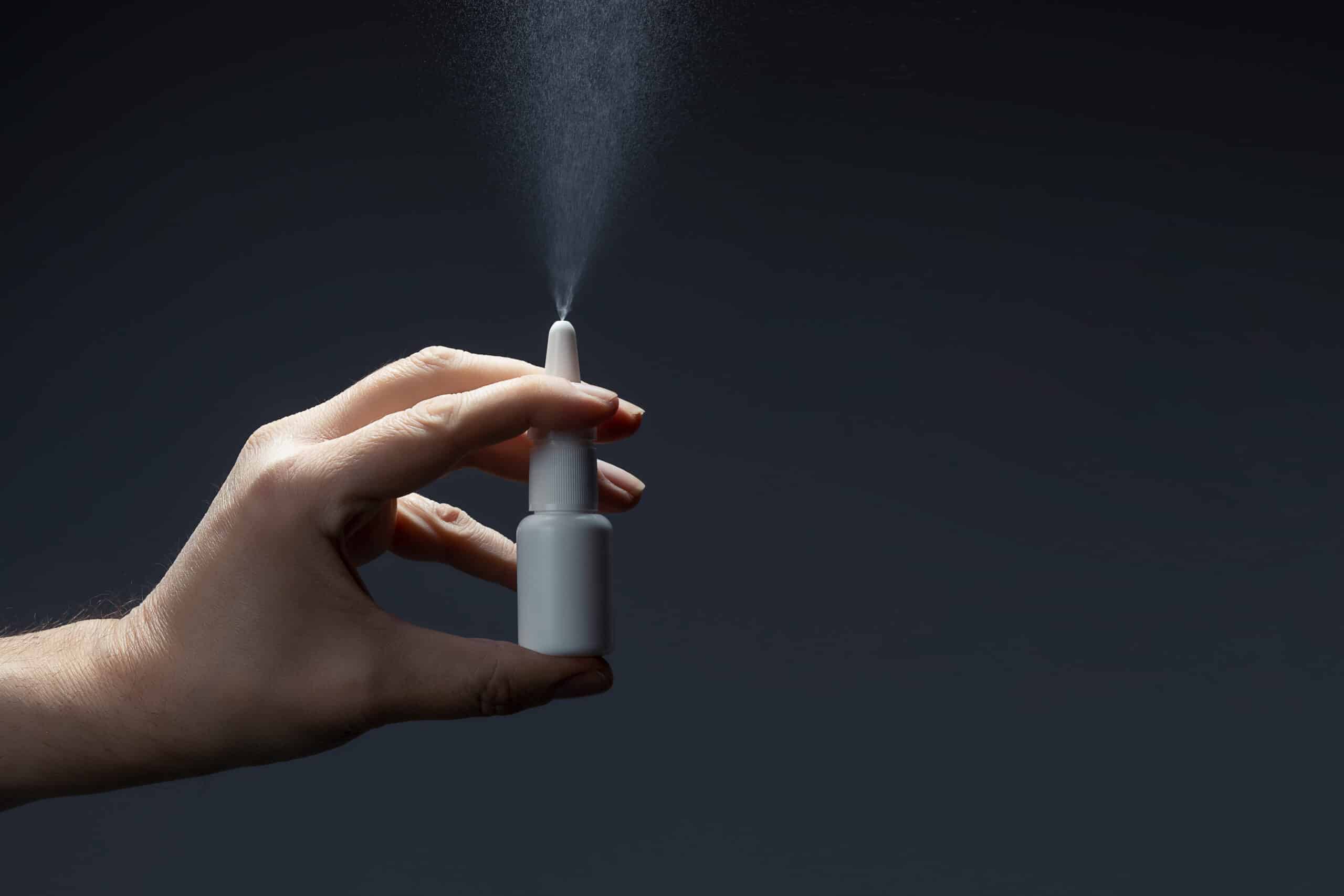 close-up of male hand using nasal spray vaccine in front of dark background