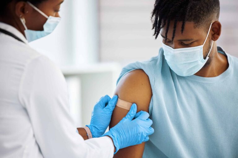 Healthcare professional wearing mask, administering vaccine to young man