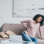 Young woman suffering from back pain, holding hand to lower back