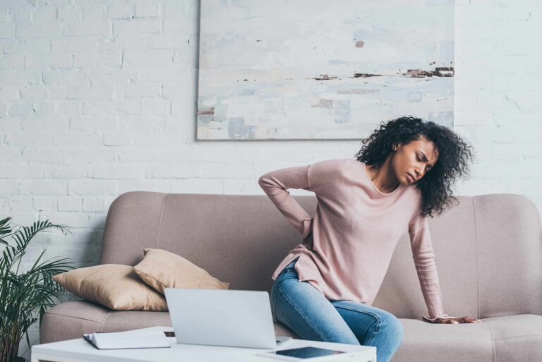 Young woman suffering from back pain, holding hand to lower back