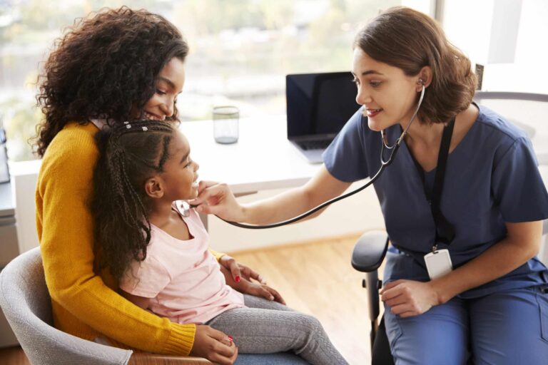 Female pediatrician listening to heartbeat of young girl sitting in her mother's lap