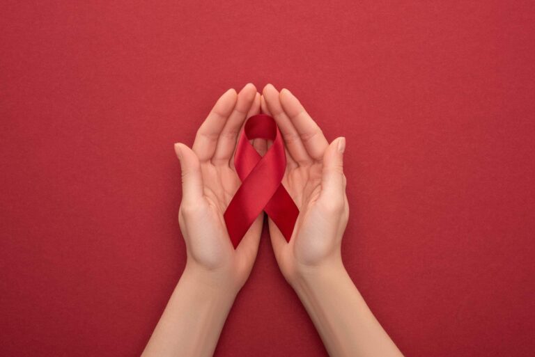 Hands holding HIV awareness ribbon, red background