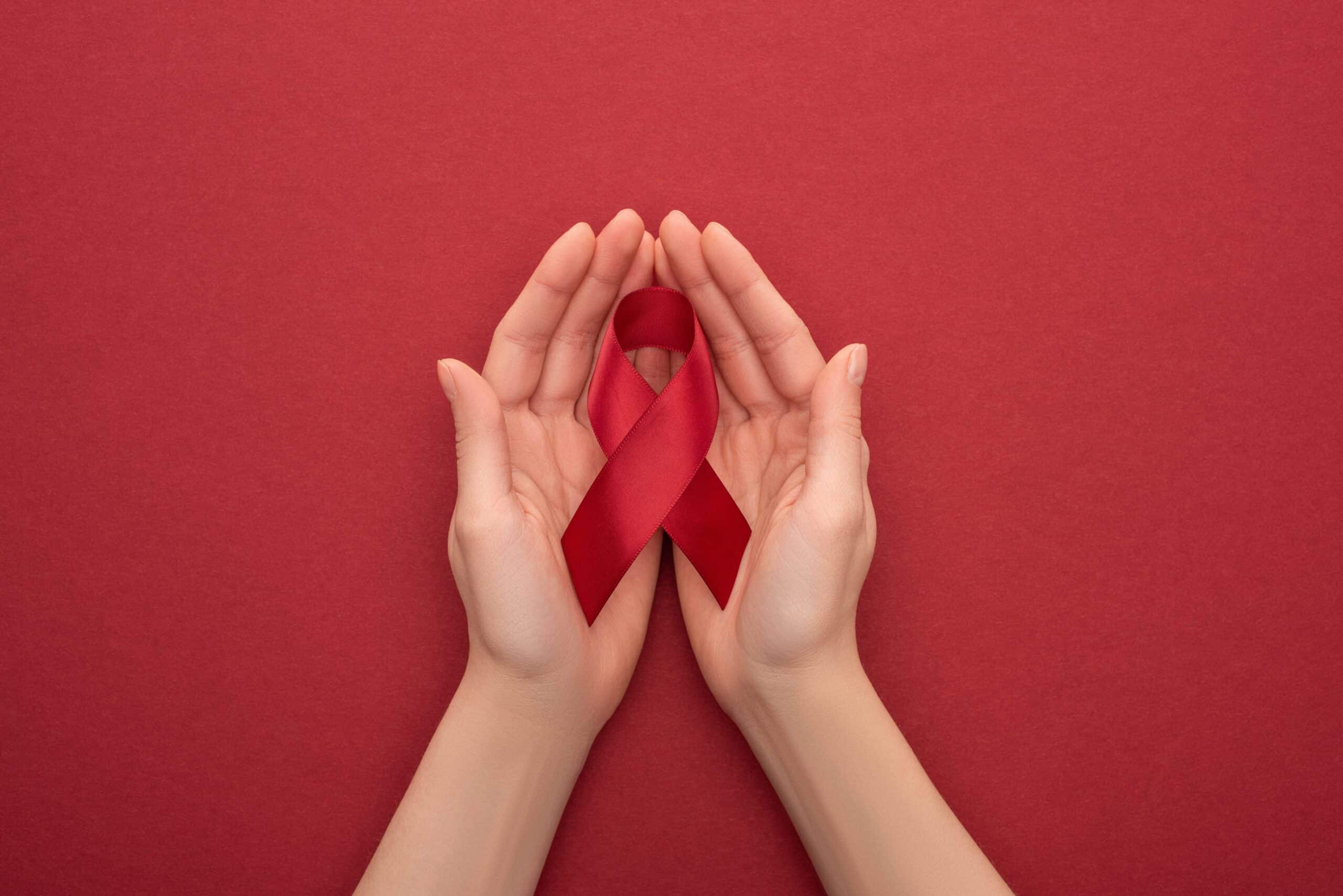 Hands holding HIV awareness ribbon, red background