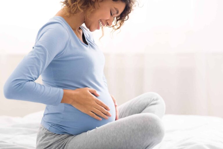 Smiling pregnant woman holding her belly while sitting