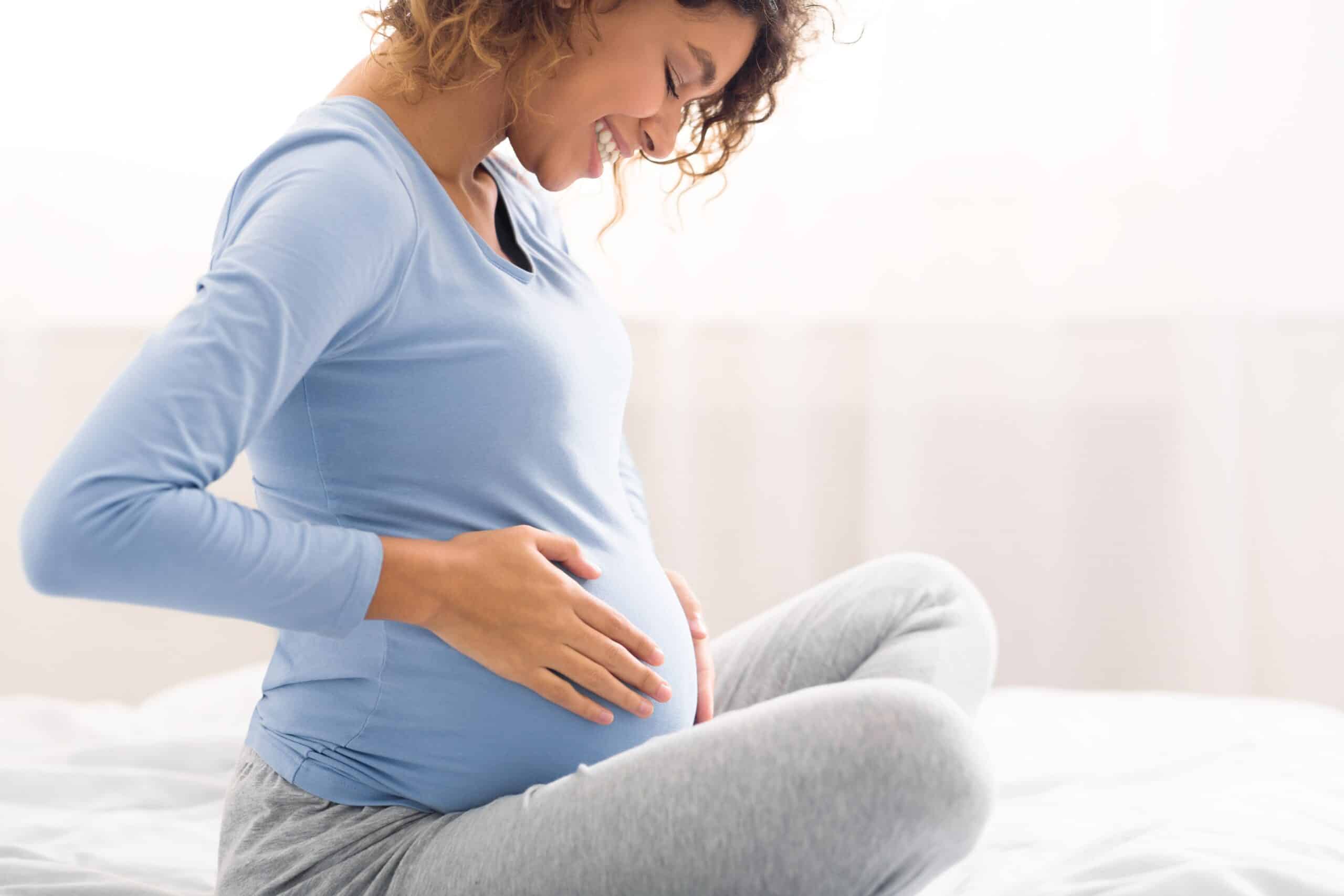 Smiling pregnant woman holding her belly while sitting