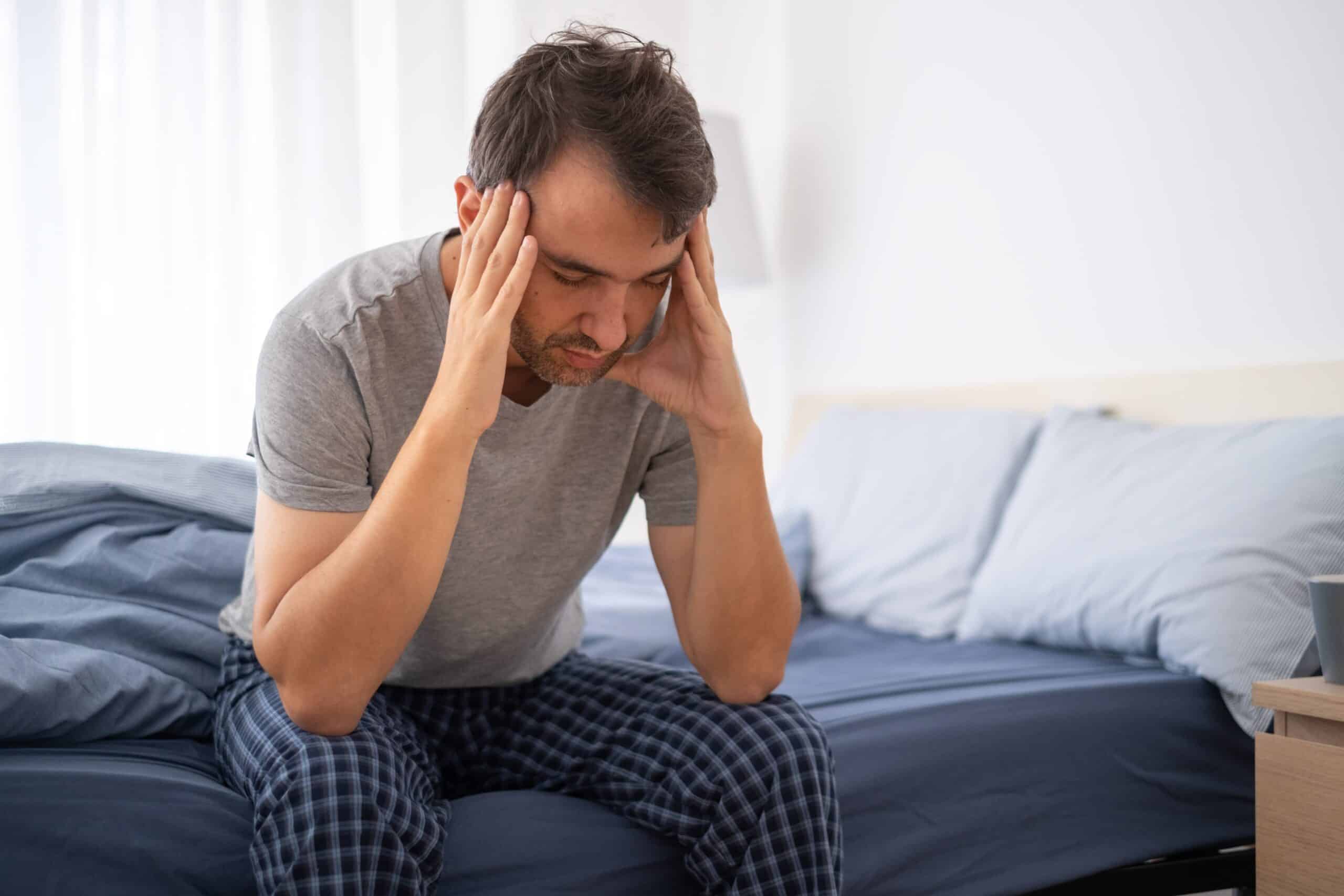 Man-sitting-on-side-of-bed-holding-head-looked-distressed-and-unwell