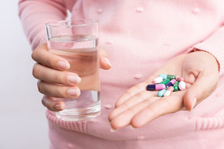 Close-up-of-woman-holding-pills-and-glass-of-water