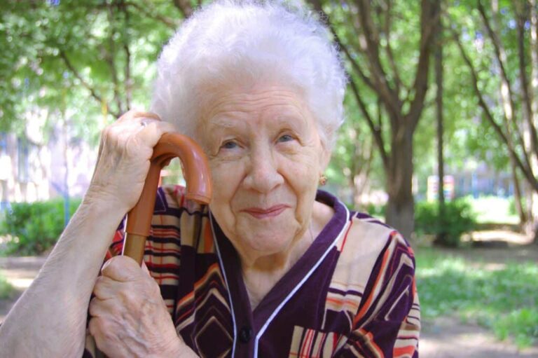 Portrait-of-smiling-senior-woman-outside-with-cane