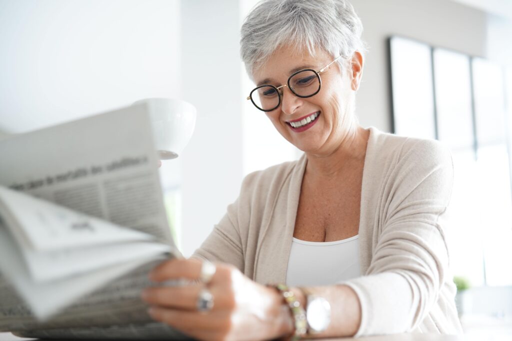 Senior-woman-smiling-while-reading-the-newspaper-at-home