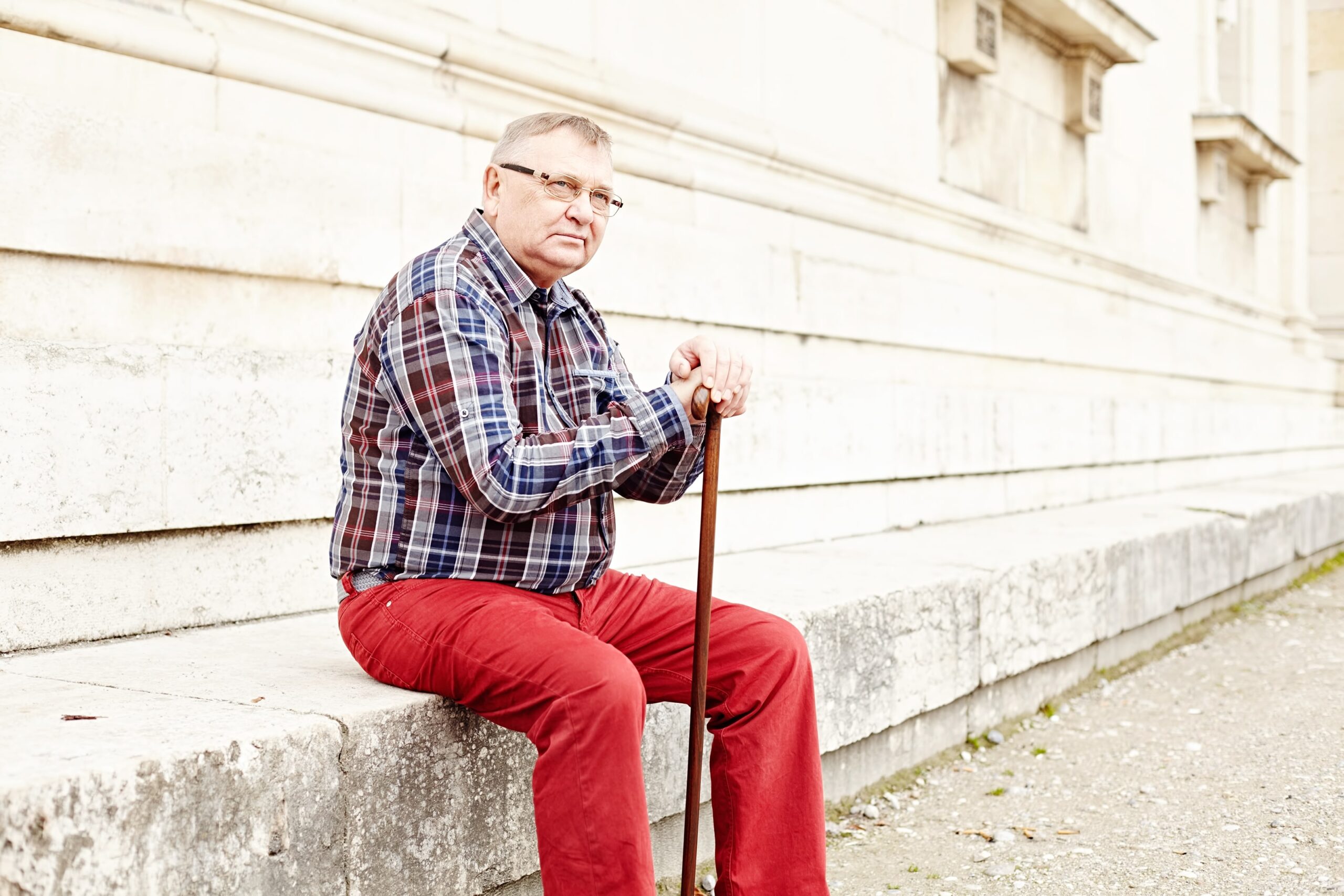 Overweight senior man sitting outside with cane