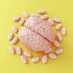 Model of human brain surrounded by pills on yellow background