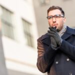 Young man dressed smartly, outside in cold weather, blowing on hands