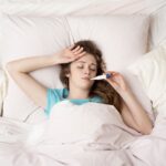 Young woman sick with the flu, in bed with thermometer
