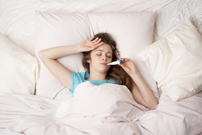 Young woman sick with the flu, in bed with thermometer