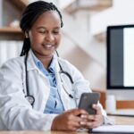Young smiling doctor looking at phone at hospital