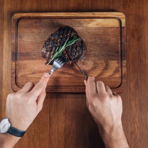 Close-up of hands using knife to cut steak