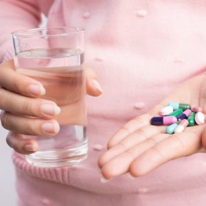 Close-up-of-woman-holding-pills-and-glass-of-water