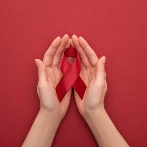 Hands holding HIV awareness ribbon, red background