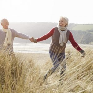 Happy older couple watching hand in hand in beach dunes