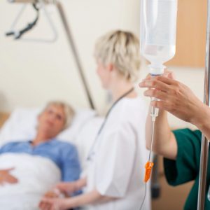 nurse adjusting infusion bottle with patient and doctor in background